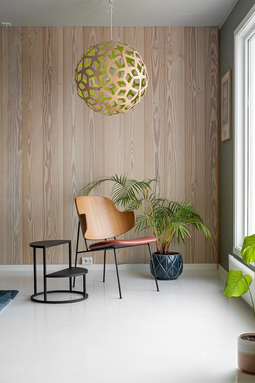 Stylish wooden chair surrounded by plants in foreground below a modern lamp in copper and greenish tones